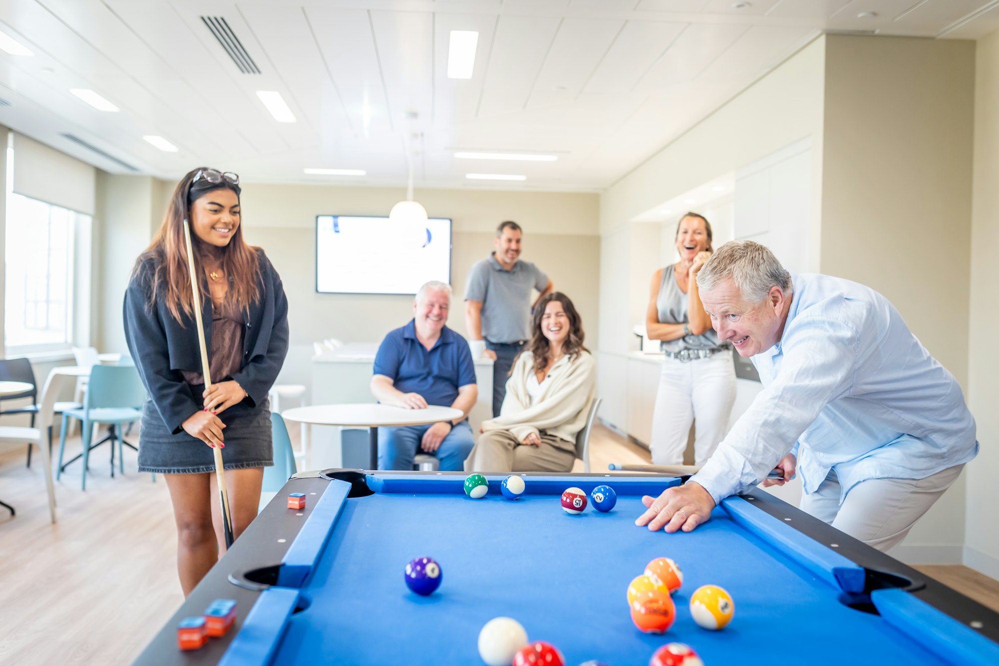 A family of several generations laughing around a pool table