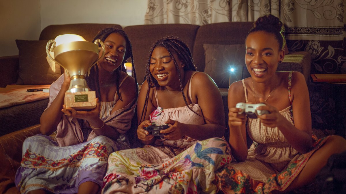 Three friends on a sofa cheering with a trophy and game controllers